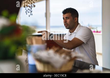 Marsa alam, ägypten 21. april 2026: Junger Mann, der ein weißes Poloshirt trägt, während eines Urlaubs in einem Restaurant im Freien in marsa alam, ägypten, zeigt und spricht Stockfoto
