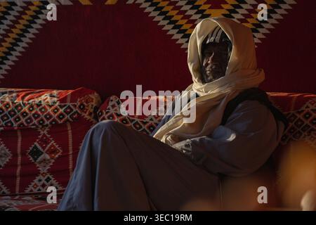 Marsa alam, ägypten 21. april 2026: Porträt eines stolzen beduinenmannes, gekleidet in galabeya und Kopftuch, entspannend auf gemusterten Kissen in marsa alam, Egyp Stockfoto