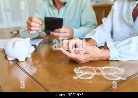 Altersvorsorge und finanzielle Absicherung für Senioren. Ein reifes Paar wird an einem Tisch gezeigt, das seine Ersparnisse mit einer Sparkasse und Geldbörse, budg, verwaltet Stockfoto