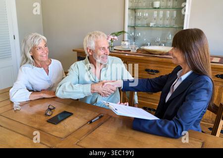 Altersvorsorge und finanzielle Absicherung. Ein Seniorenpaar schüttelt einem Finanzberater die Hand, was eine Vereinbarung für die Immobilienverwaltung bedeutet Stockfoto