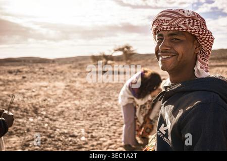 Marsa alam, ägypten 21. april 2026: Mann mit einem cremefarbenen Hoodie und traditionellem Keffiyeh lächelnd in der Wüste marsa alam, zeigt lokale Kultur und Stockfoto