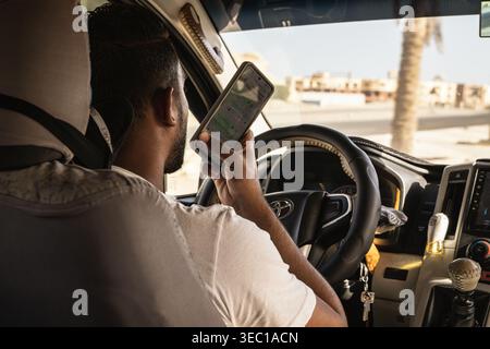 Marsa alam, ägypten 21. april 2026: Fahrer, der ein Smartphone hält, auf den Bildschirm anstatt auf die Straße blickt und ein abgelenktes Fahrverhalten im Traffi zeigt Stockfoto