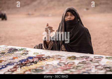 Marsa alam, ägypten 21. april 2026: beduinenfrau in Niqab verkauft traditionelle handgefertigte Armbänder an einem Wüstenmarkt in marsa alam, ägypten — Lokal A Stockfoto