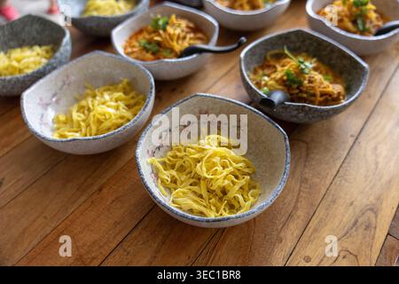 Köstliche traditionelle Nord-Thai-Curry-Nudeln khao Soi in Keramikschale auf hölzernem Blick auf den Tisch vorbereiten warme einladende Atmosphäre von Einheimischen Stockfoto