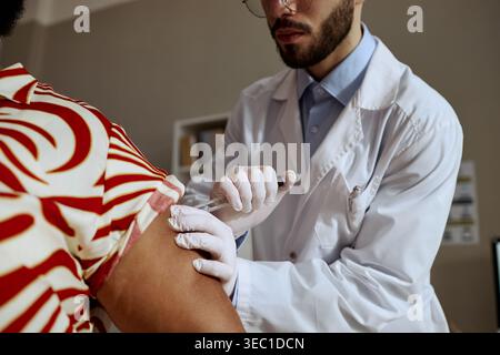 Männlicher Arzt verabreicht Impfstoff an Schwarze Frau in der Klinik Stockfoto