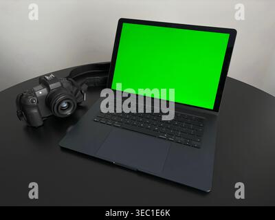 Laptop mit grünem Bildschirm und Digitalkamera auf schwarzem Schreibtisch Stockfoto