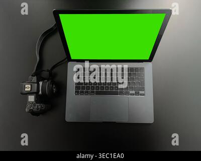 Laptop mit grünem Bildschirm und Digitalkamera auf schwarzem Schreibtisch Stockfoto