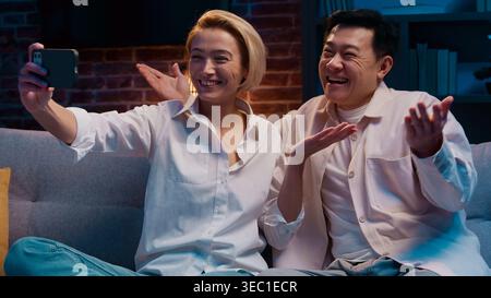 Glückliche multirassische Paare sprechen Videoanruf mit Handy lächelnd Talk Konferenz verheiratete Ehepartner verschiedene asiatische Männer und weiße Frau positiv Stockfoto