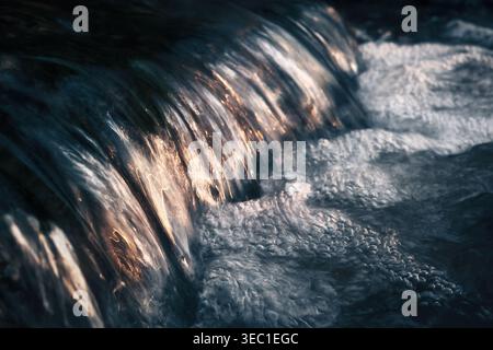 Schönheit der Natur: Nahaufnahme eines kleinen Wasserkaskaden auf einem natürlichen Fluss, der das angenehme Sonnenlicht reflektiert Stockfoto