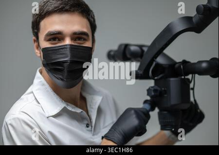 Porträt des männlichen Zahnarztes in Maske, die in der Nähe des Zahnmikroskops steht Stockfoto