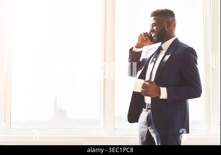 Attraktive Geschäftsmann Gespräch per Telefon und Kaffee trinken in der Nähe der Fenster Stockfoto