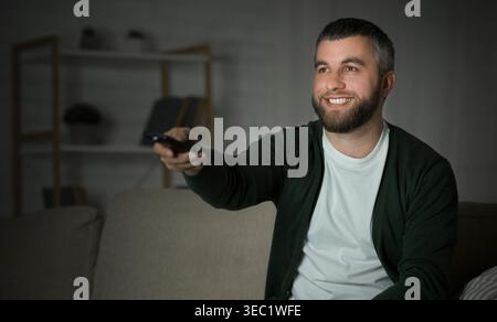 Man sieht Fernsehen und genießt seinen Abend zu Hause mit einer Fernbedienung in der Hand Stockfoto