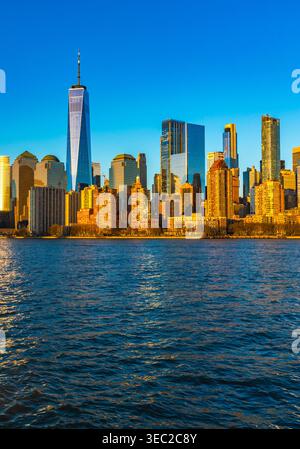 Das goldene Sonnenlicht schimmert auf dem Wasser von Lower Manhattan und zeigt die atemberaubende Skyline von New York City und die majestätischen Gebäude. Stockfoto