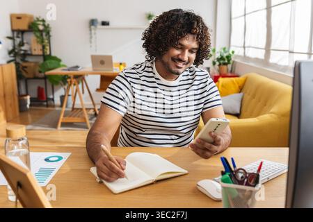 Junger indischer Mann, der mit Smartphone am Schreibtisch lernt Stockfoto