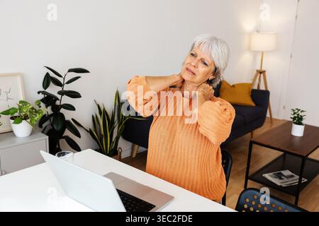 Gestresste, reife Geschäftsfrau mit Nackenschmerzen, die zu Hause am Laptop arbeitet Stockfoto