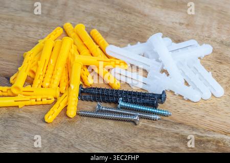 Wandanker aus Kunststoff und Metallschrauben auf einer Holzoberfläche, die übliche Befestigungsteile für Wandmontage, Hausreparaturen und Bauarbeiten zeigen Stockfoto