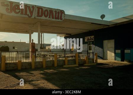 Verlassenes Jelly Donut Drive-in-Gebäude in der kalifornischen Wüste entlang der historischen Route 66 mit langen Schatten und leerem Parkplatz unter blauem Himmel. Stockfoto