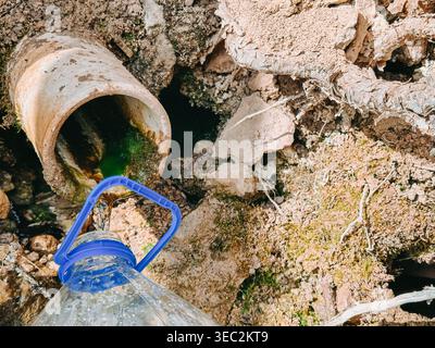 Nahaufnahme von verunreinigtem Wasser, das aus einer beschädigten Leitung in einen Kunststoffbehälter abläuft. Hebt Umweltverschmutzung, unsichere Wasserquellen und pu hervor Stockfoto