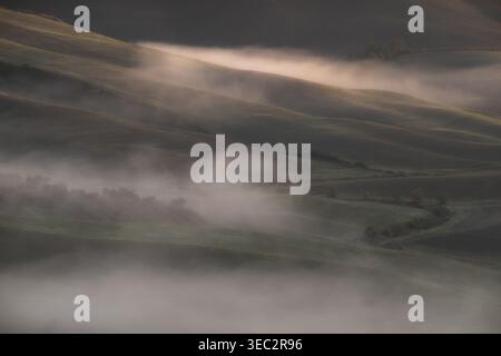 Blick aus einem hohen Winkel auf nebelige Hügel und Täler während des frühen Morgenlichts. Niedrige Wolken und Nebel über ländlicher Landschaft. Stockfoto