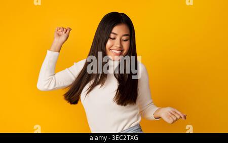 Die junge Frau tanzt freudig vor einem leuchtend gelben Hintergrund und drückt Glück und Freiheit aus Stockfoto