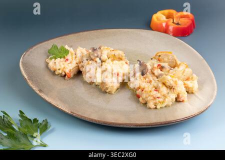 Köstliches cremiges Risotto mit Huhn und Pilzen auf einer Keramikplatte serviert, garniert mit frischer Petersilie und Paprika. Stockfoto