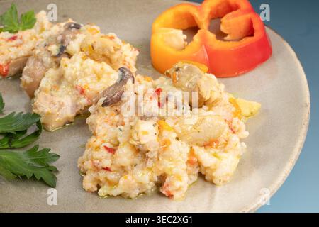 Nahaufnahme eines köstlichen cremigen Risottos mit Huhn und Pilzen auf einer Keramikplatte, garniert mit Paprika und Petersilie. Stockfoto
