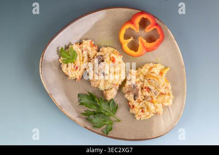 Handwerklich hergestellte Keramikplatte, die drei Haufen cremiger Hühnerpilzrisotto enthält. Frische Petersilie und ein geformter roter Pfefferring sind Garnituren. Stockfoto