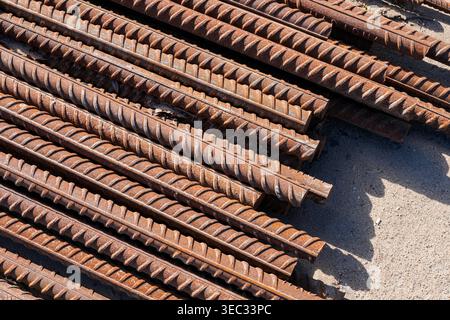 Gestapelte Bewehrungsstäbe aus rostigem Stahl auf der Baustelle, die für Betonarbeiten bereit sind Stockfoto