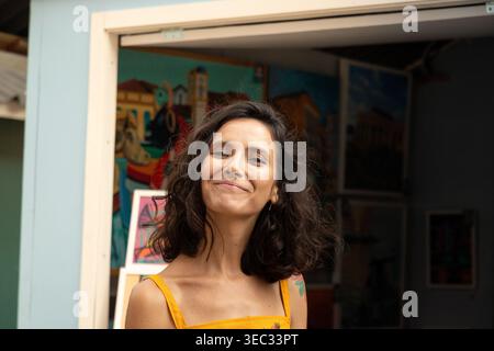 Eine junge Frau mit gewelltem braunem Haar lächelt vor einer Kunstgalerie in die Kamera Stockfoto