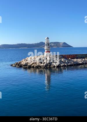 Leuchtturm an felsiger Küste mit blauem Meer und klarem Himmel, geeignet als Hintergrundbild. Mobiles Foto Stockfoto