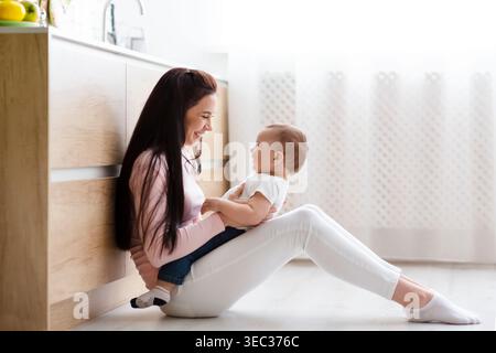 Mutter genießt freudige Momente mit Baby am sonnigen Nachmittag auf Küchenboden Stockfoto