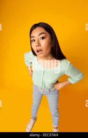 Junge Frau in hellgrünem Oberteil posiert spielerisch vor hellgelbem Hintergrund Stockfoto