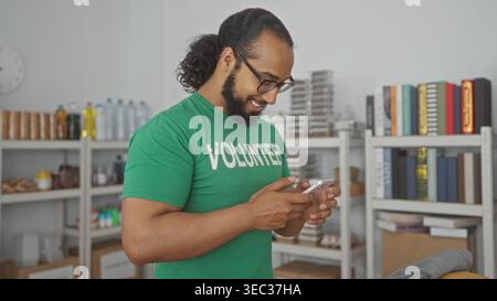 Ein Freiwilliger hält ein Smartphone und tippt mit beiden Händen im Spendengebäude, lächelt beim Lesen von Nachrichten; Unterstützung der Mitgefühl-Community. Stockfoto