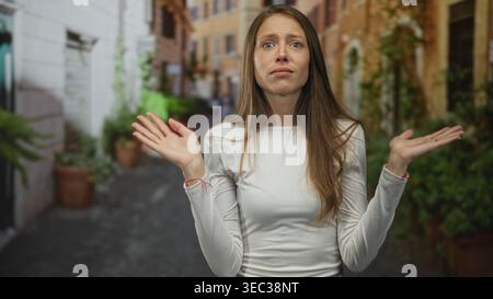 hispanische Frau mit erhobenen Händen und überraschtem Gesicht auf einer engen Straße, die von Topfpflanzen und alten Gebäuden gesäumt ist; überraschendes Verwirrungswunder. Stockfoto
