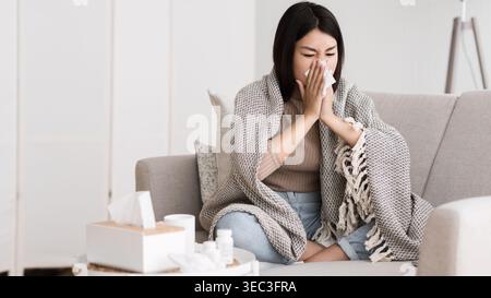 Frau, die auf der Couch sitzt und sich unwohl fühlt, während sie in Decke gehüllt ist Stockfoto