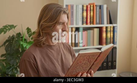 Mann, der ein reich verziertes Hardcover-Buch mit Fingern auf Seiten hält, steht und liest in einem mit Bücherregalen und Ordnern gesäumten Arbeitszimmer; Besinnung. Stockfoto