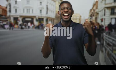 Mann mit geballten Fäusten, schreiend und lachend auf einer belebten europäischen Straße, mit Brille und Marinepolo, mit aufgerissenem Mund in einer kurzen Sequenz; Stockfoto