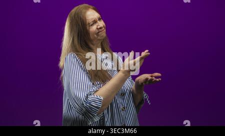 Frau Senior hispanic zeigt Zeigefinger mit gefaltetem Arm, sichtbarem Unterarm und Hand, trägt ein blau gestreiftes Hemd im lila Studio-Hintergrund; Missbilligung Stockfoto