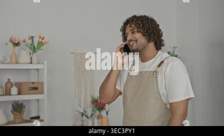 Mann, der das Smartphone am Ohr hält, Hand auf der Brust im Studio-Blumenladen trägt eine Schürze und spricht am Telefon; ruhiger Service. Stockfoto