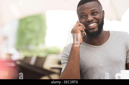 Fröhlicher Mann, der am Telefon in einem Café im Freien in einer sonnigen Umgebung spricht Stockfoto