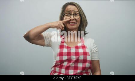 Eine ältere Frau mit roter Karomuster und Brille zeigt mit dem Finger an die Nase und lächelt direkt in die Kamera im Studio; warme Hausmannskost. Stockfoto