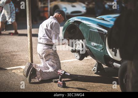 Ein Mechaniker kniet neben einem Oldtimer und arbeitet mit einem Elektrowerkzeug am Vorderrad Stockfoto