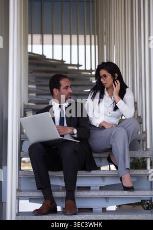 Geschäftskollegen, die ein Meeting auf einer Bürotreppe mit Laptop in einem modernen Arbeitsbereich durchführen Stockfoto