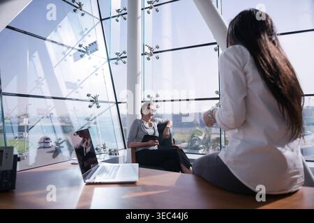 Kollegen aus dem Nahen Osten, die ein zwangloses Geschäftstreffen in einem modernen, offenen Startup-Büro mit Blick auf die Stadt abhalten Stockfoto