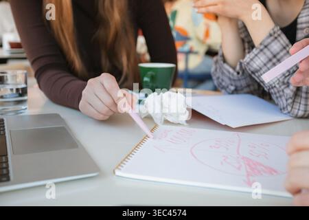 Nahaufnahme von drei Frauen, die an einem Tisch in einem Café sitzen und handgezeichnete Diagramme und Diagramme in einem Notizbuch während eines Geschäftstreffens analysieren Stockfoto