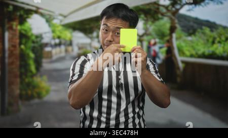 Der Schiedsrichter trägt ein gestreiftes Trikot, hält die gelbe Karte und zeigt mit dem Finger auf die Straße. Stockfoto