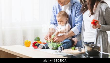 Gemeinsam kochen in einer hellen Küche mit einem Baby, das Gemüse genießt Stockfoto