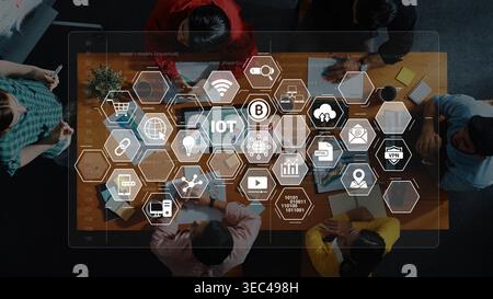 Ein vielseitiges Team nimmt an einem strategischen Meeting Teil und analysiert IoT-Technologie mit digitalen Symbolen, die auf einem modernen Arbeitstisch angezeigt werden Stockfoto