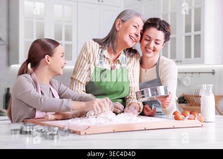 Glückliche Großmutter, ihre Tochter und Enkelin kochen zusammen am Tisch in der Küche Stockfoto