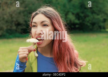 Eine junge Frau mit rosa Haaren, die draußen einen rohen Pilz essen will. Stockfoto